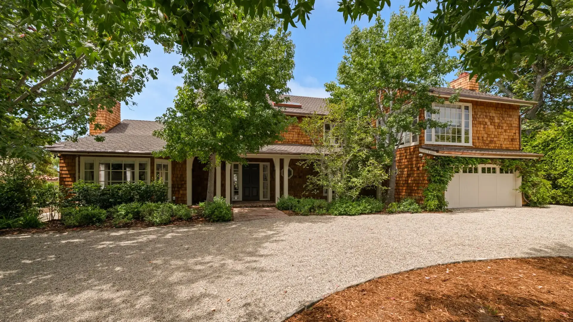 Charming house entrance with lush greenery and a gravel driveway.